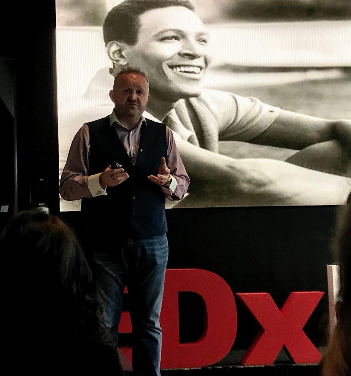 Perry Timms speaking on stage at a TEDx event